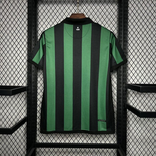 Green and black striped Celtic 06/07 away shirt hanging on a rack with a grid pattern.
