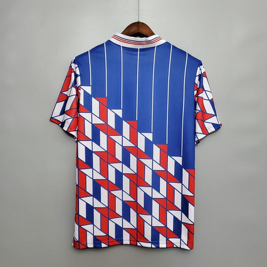 Colorful geometric patterned Ajax 89/90 away shirt on a hanger against a gray background