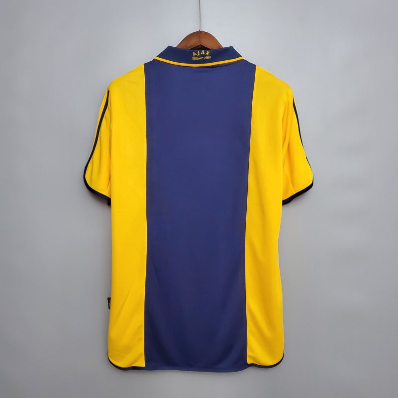 Yellow and blue Ajax 00/01 away shirt on a hanger against a gray background