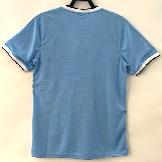 Light blue Man City 13/14 home shirt with black trim on a beige background