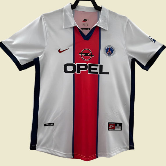 White PSG 98/99 away shirt with red and blue accents, featuring Nike and Opel logos, on a white background.