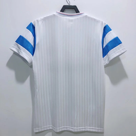 White Marseille 90/91 home shirt with blue accents on a hanger against a white background