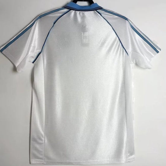 White Marseille 98/99 centenary home shirt with blue accents on a hanger against a white background