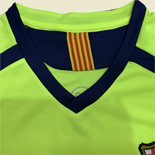 Close-up of a bright green Barcelona 05/06 away shirt  with a red and yellow striped detail and a logo on a dark background.
