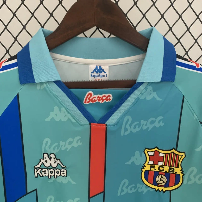 Teal Barcelona 96/97 long sleeve away shirt with Kappa and Barça logos on a hanger against a chain-link fence background.