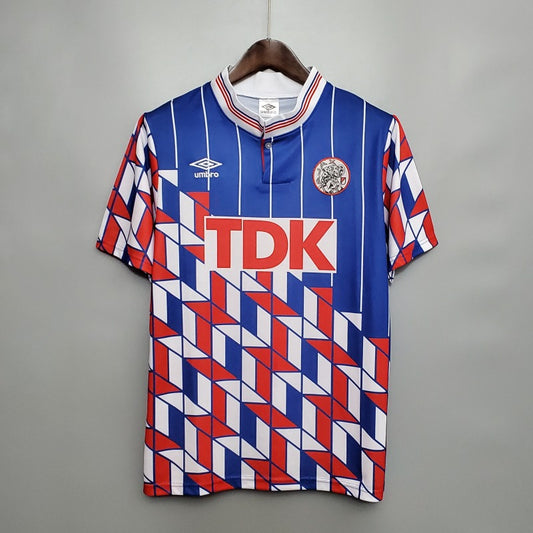 Colorful Ajax 89/90 away shirt with geometric pattern and 'TDK' branding on a gray background