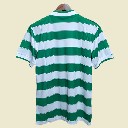 Green and white striped Celtic 85/86 home shirt on a hanger against a black background
