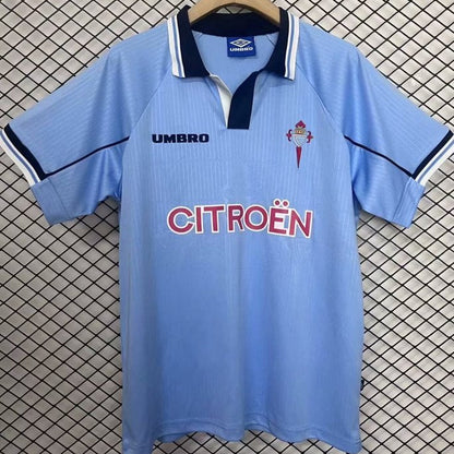 Blue Celta Vigo 97/98 home shirt with Umbro and Citroén logos on a hanger against a checkered background