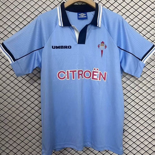 Blue Celta Vigo 97/98 home shirt with Umbro and Citroén logos on a hanger against a checkered background