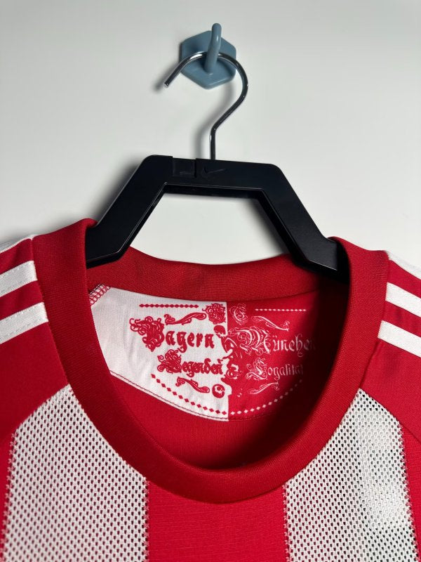 Red and white Bayern Munich 10/11 home shirt with a brand logo on a hanger against a white background