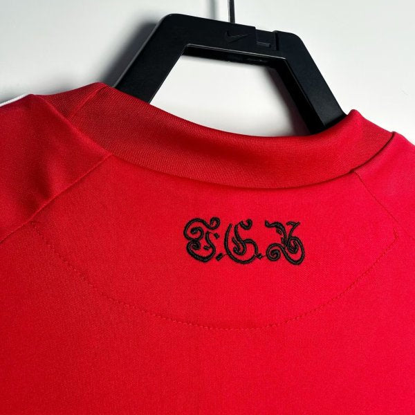 Red Bayern Munich 10/11 home shirt with black logo on a hanger against a white background