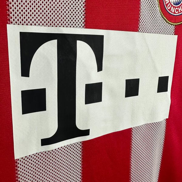 Close-up of a Bayern Munich 10/11 home shirt with a logo and text on a red and white striped background