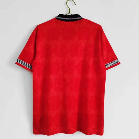 Red England 1990 away shirt with black collar and sleeve details on a hanger against a white background