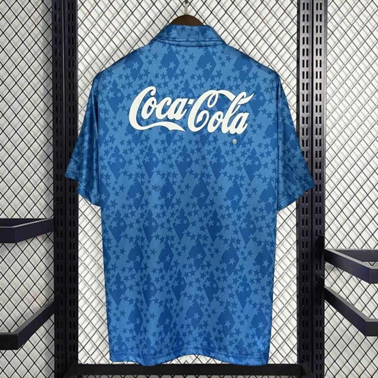 Blue 93-95 cruzeiro home shirt with Coca-Cola logo on a hanger against a patterned wall.