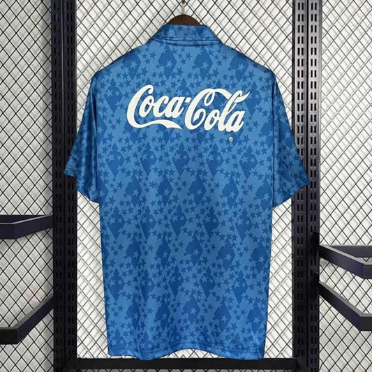 Blue 93-95 cruzeiro home shirt with Coca-Cola logo on a hanger against a patterned wall.