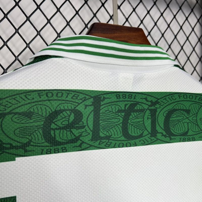 Celtic 95-97 home shirt with green accents and 'Celtic' branding on a hanger against a chain-link fence background.
