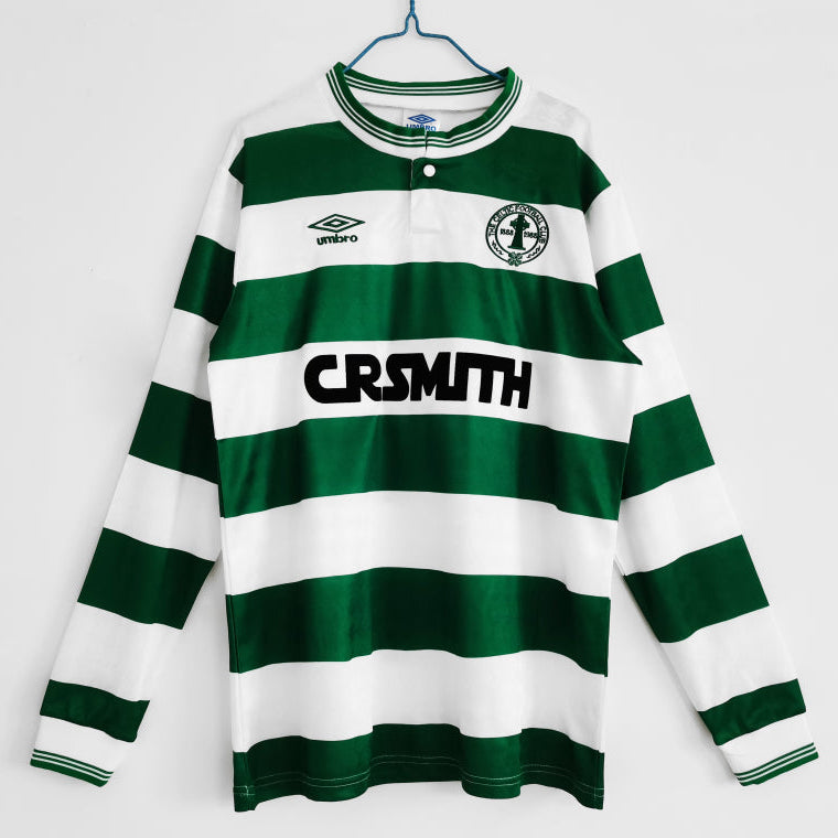Green and white striped Celtic 87/88 long sleeve home shirt with 'CR SMITH' branding on a hanger against a white background