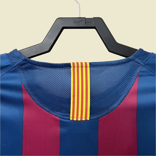 Blue and red Barcelona 05/06 champions league shirt  with a yellow stripe on a hanger against a white background