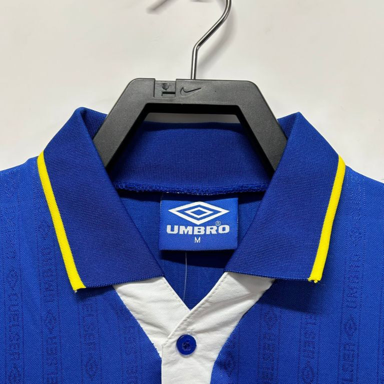 Blue Chelsea 95-97 home shirt with yellow accents on a hanger, featuring Umbro branding.