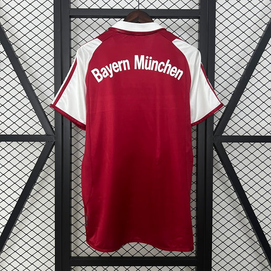 Red Bayern Munich 03/04 home shirt with 'Bayern München' text on a black and white checkered background