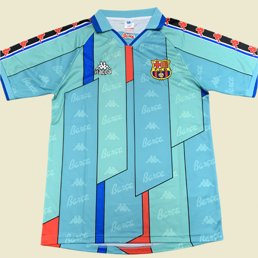 Light blue Barcelona 96/97 away shirt with red and black accents, featuring Barca logo, on a gray textured background.