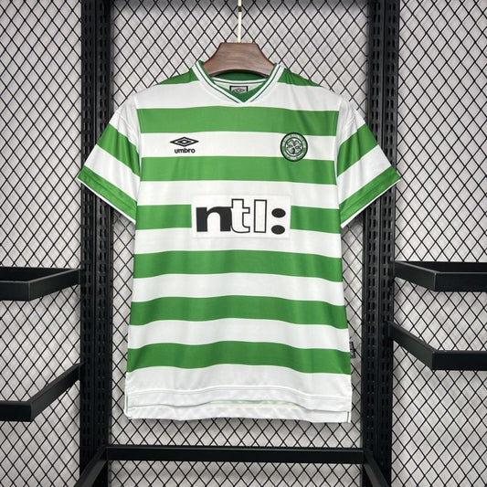 Green and white striped 99/00 Celtic home shirt with visible branding on a hanger against a black grid background.