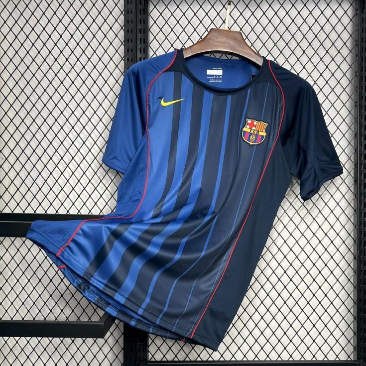 Blue Barcelona 04/05 away shirt with a logo on a hanger against a grid background