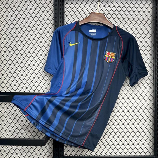 Blue Barcelona 04/05 away shirt with a logo on a hanger against a grid background