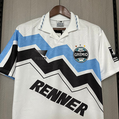 White 95/96 Gremio away shirt with blue and black zigzag pattern, featuring 'Renner' and 'Gremio' logos, on a hanger.