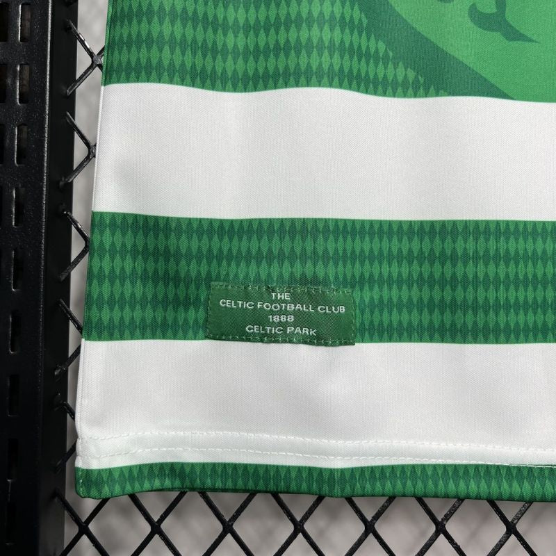 Green and white Celtic 98/99 home shirt with Celtic Football Club label on a black chain-link fence background