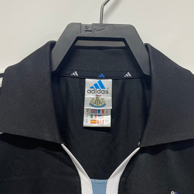 Black Newcastle 00/01 away shirt with Adidas and Newcastle United logos on a hanger against a white background