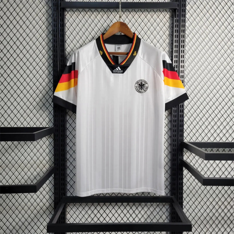 White Germany 1992 home shirt with black, red, and yellow stripes hanging on a rack.