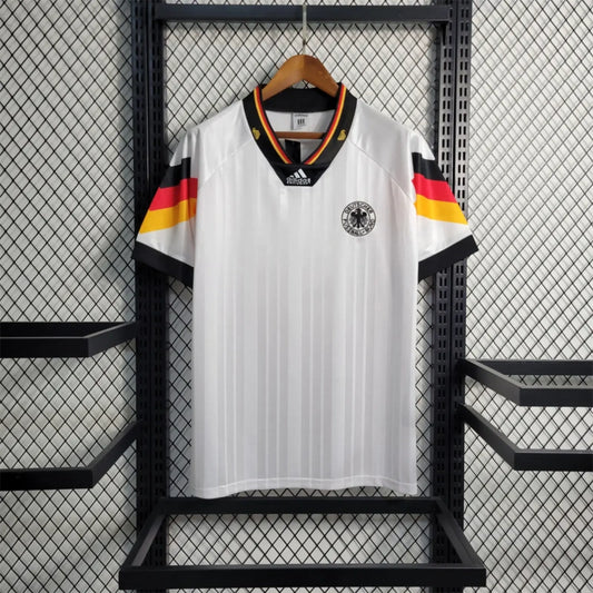 White Germany 1992 home shirt with black, red, and yellow stripes hanging on a rack.