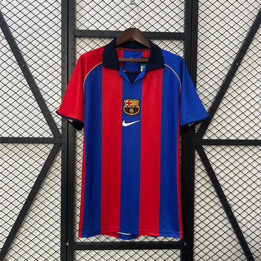 Red and blue Barcelona 01/02 home shirt with a logo on a hanger against a black grid background