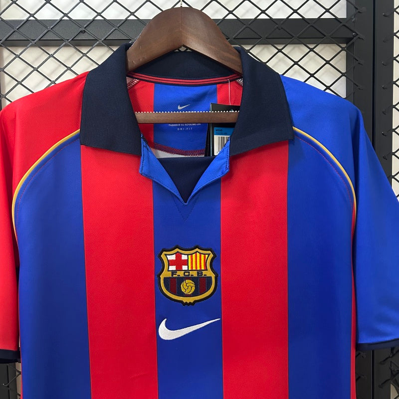 Red and blue Barcelona 01/02 home shirt with Nike logo on a hanger against a metallic background