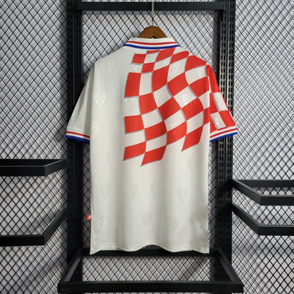 White Croatia 1998 home shirt  with red and blue checkered design on a hanger against a black metal rack.
