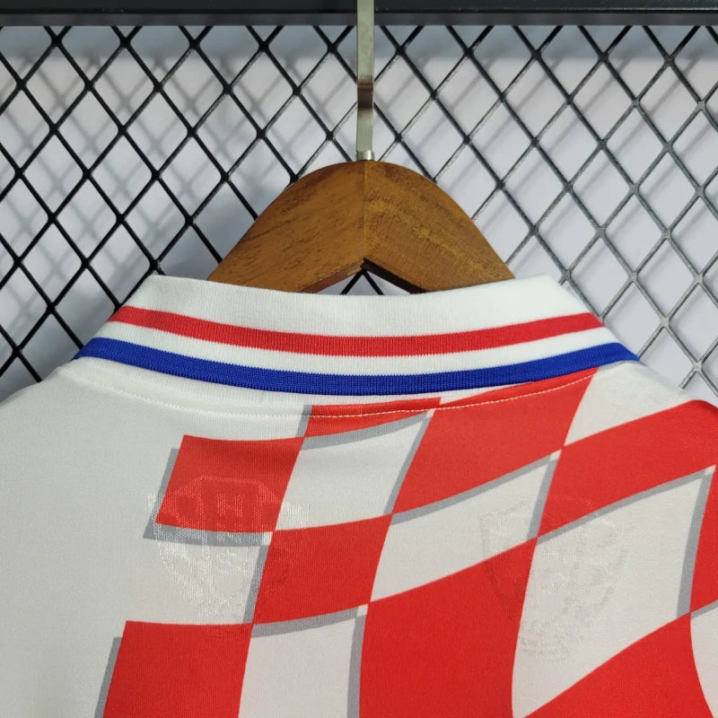 Red, white, and blue checkered Croatia 1998 home shirt  on a hanger against a chain-link fence background