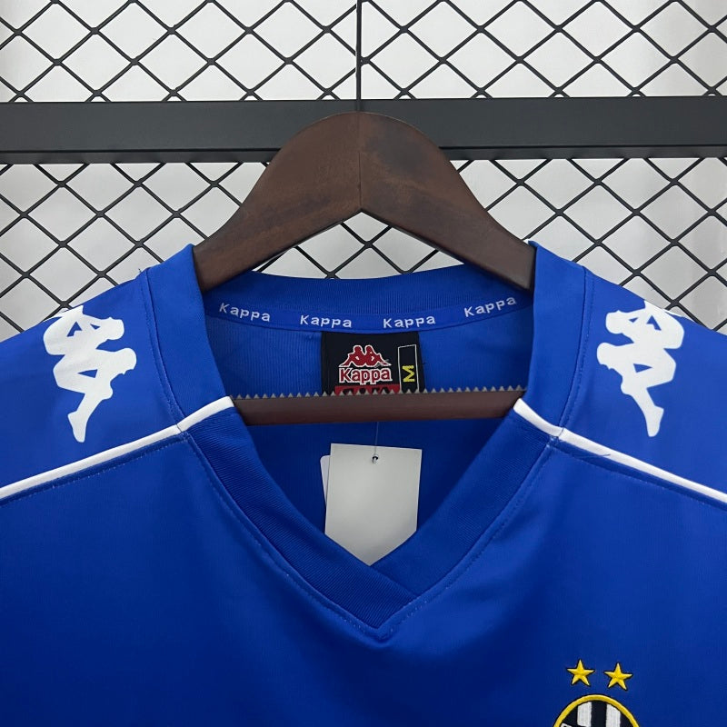 Blue Juventus 99/00 away shirt  with white accents on a hanger against a checkered background