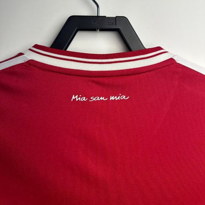 Red Bayern Munich 13 champions league final shirt with white stripes and 'Mia san mia' text on a hanger against a light gray background