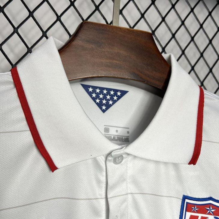 White USA 2014 home shirt with red and blue accents on a hanger against a chain-link fence background.