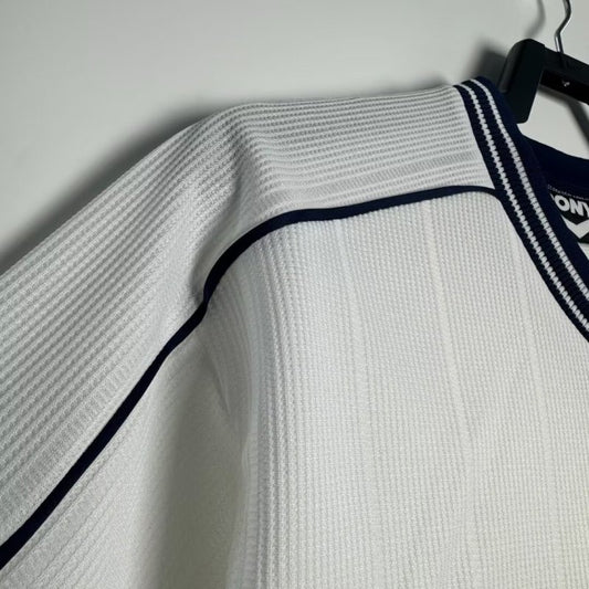 White Tottenham Hotspur 97-99 home shirt with black trim hanging on a hanger against a gray background