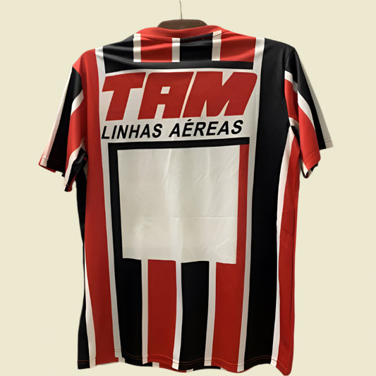 Red, black, and white striped São Paulo 93-94 away shirt with 'TAM Linhas Aéreas' logo on a dark background