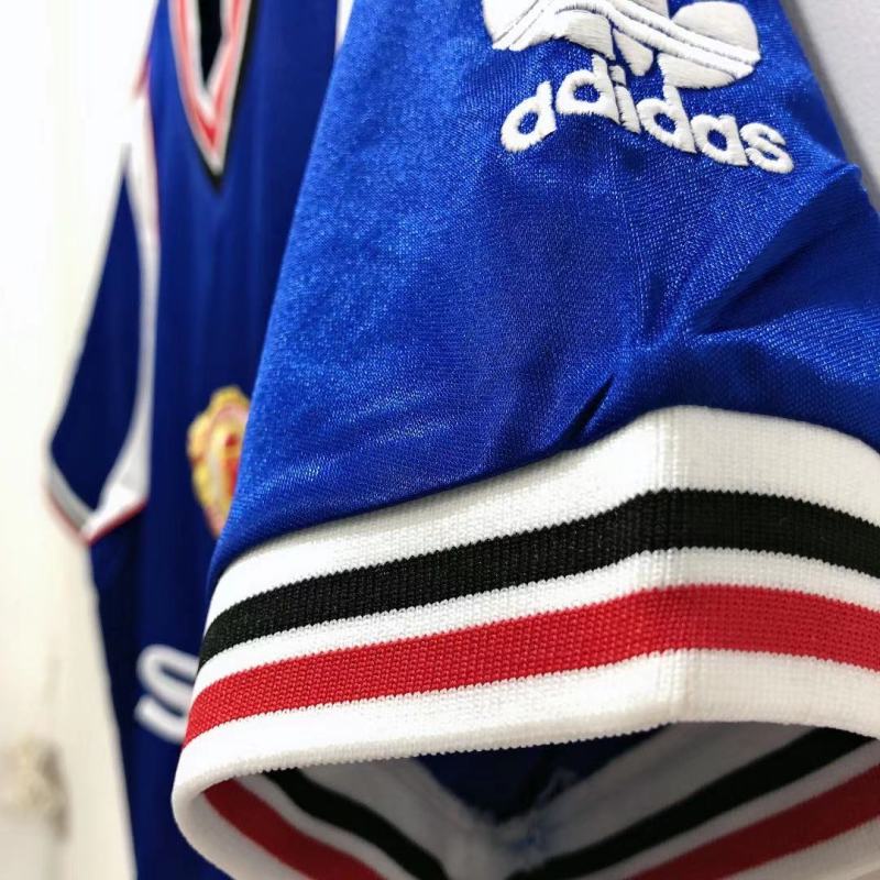 Close-up of a blue Man united 85/86 third shirt with Adidas logo and red, white, and black striped trim.