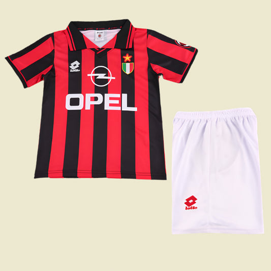 Red and black striped ac Milan 96/97 kids kit with Opel logo and white shorts on a textured gray background