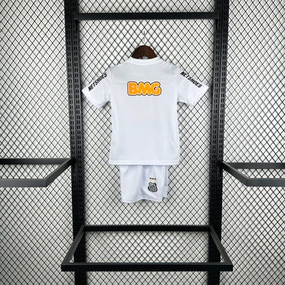 White Santos 2012 centenary home kids kit with orange logo on a black metal rack against a gray wall.