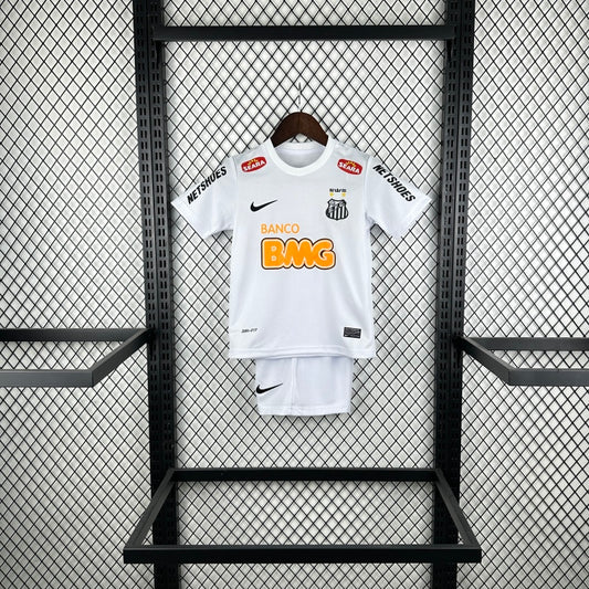 White Santos 2012 centenary home kids kit with branding on a black metal rack against a patterned wall.