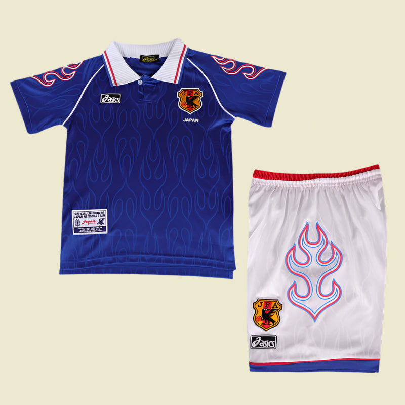 Blue Japan 1998 home kids kit with red and blue flame design on a textured gray background