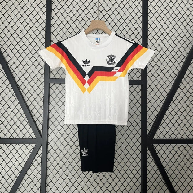 White Adidas Germany 90 World Cup home kids kit  with colorful stripes and black shorts on a hanger against a grid background