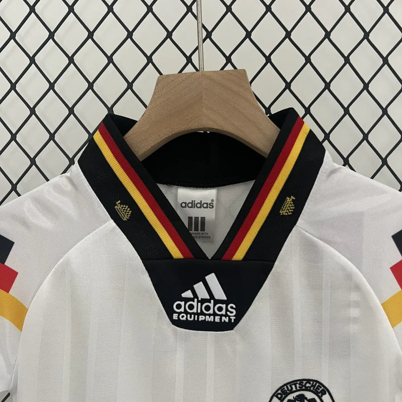 White Germany 1992 home kids kit with black Adidas Equipment collar against a chain-link fence background