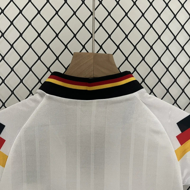White Germany 1992 home kids kit with red, yellow, and black striped collar against a chain-link fence background